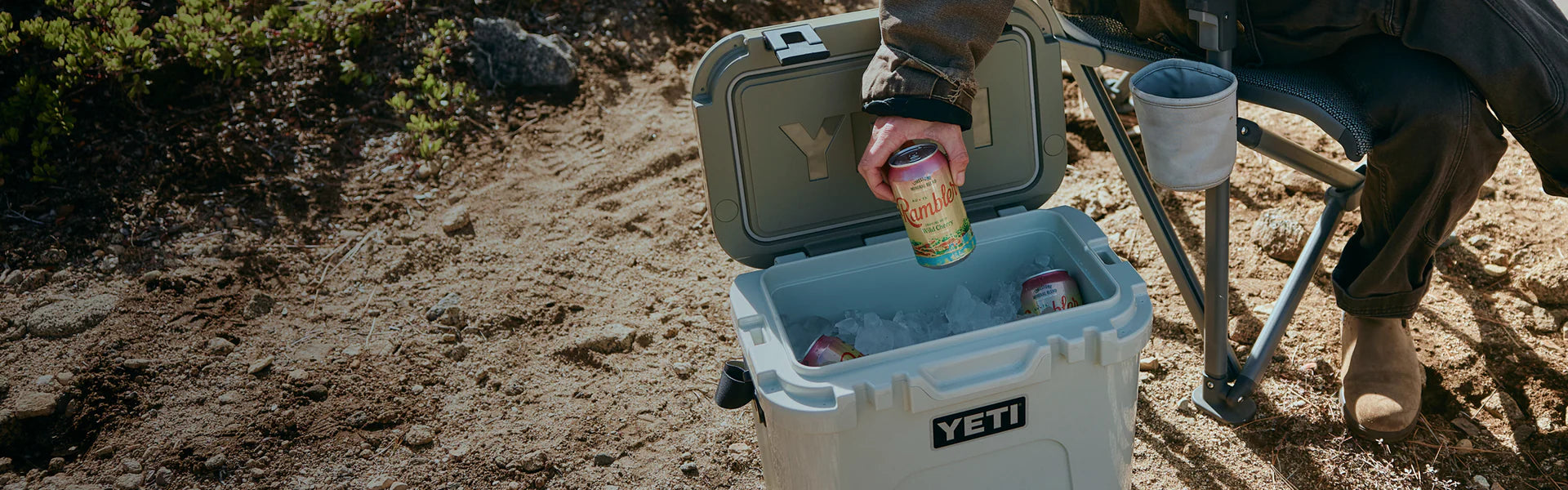 Person opening a YETI cooler outdoors with a can of beer.