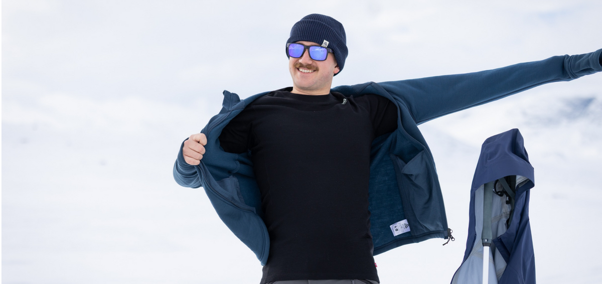 Man wearing an Aclima WarmWool merino base layer, taking off his fleece jacket in the snow