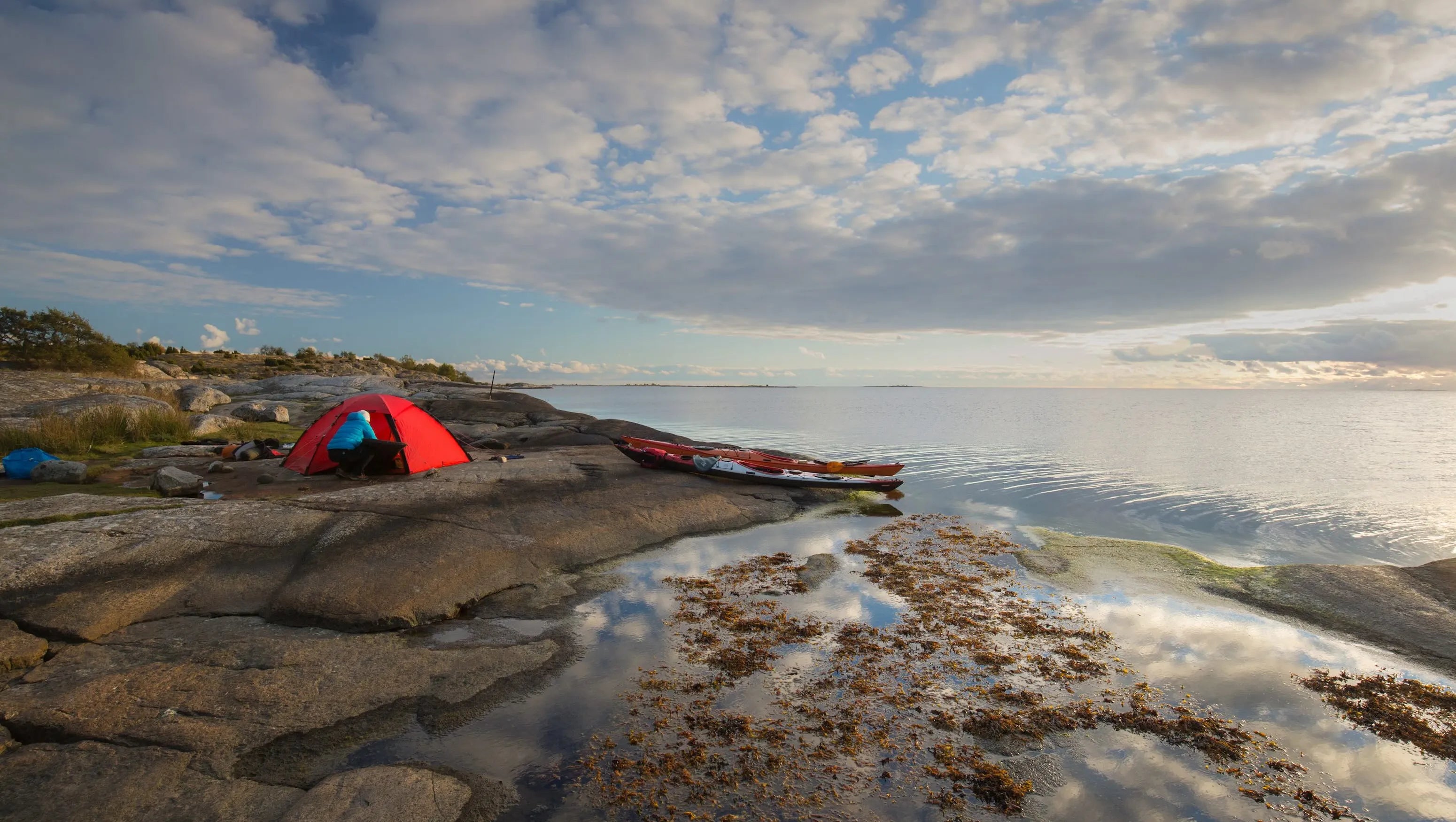 Rotes Hilleberg-Zelt auf Felsen neben einem See mit Kajaks aufgestellt